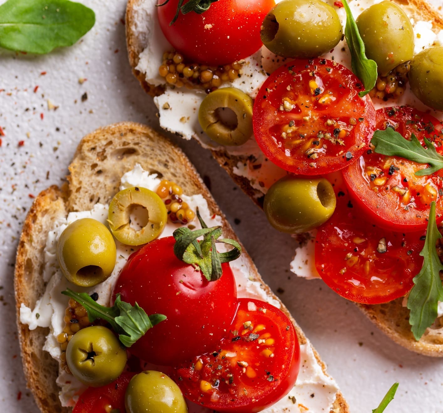 Whole-grain toast topped with creamy ricotta, fresh tomatoes, olives, and arugula—a vibrant example of a Mediterranean-inspired appetizer