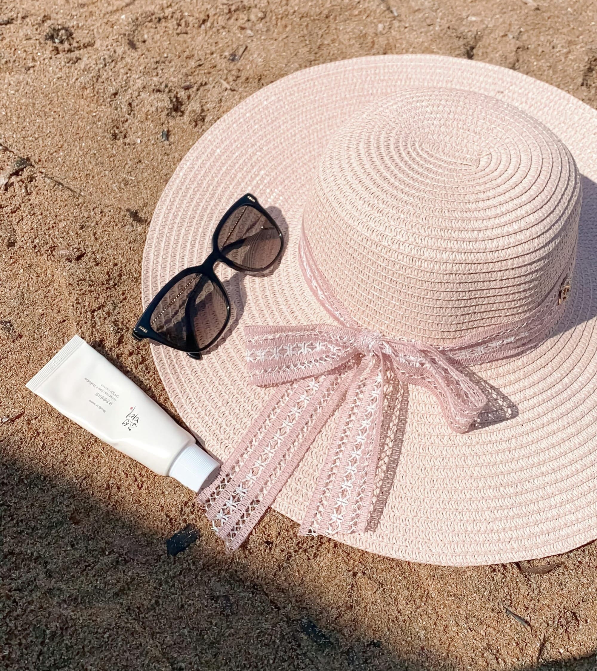 Sand close-up with sunglasses, suncreme and straw hat