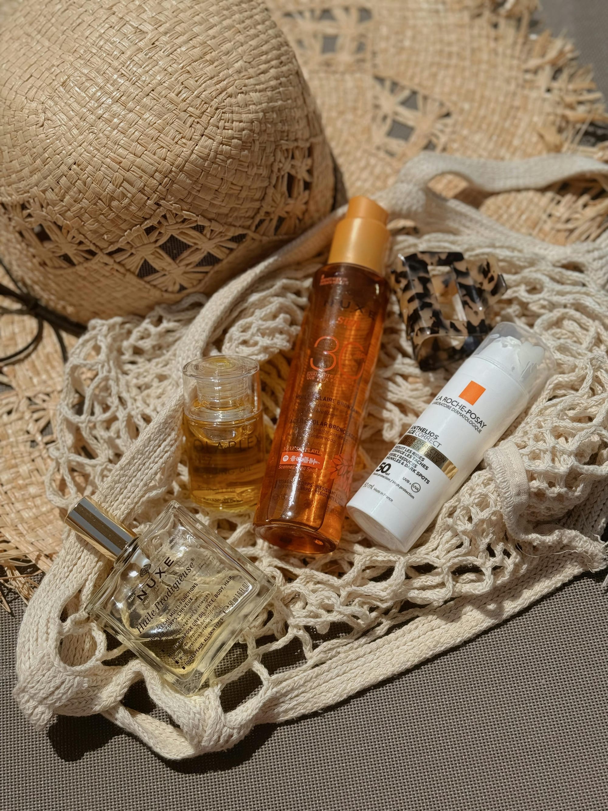 Close up of woven tote, straw hat, sun oil and different sun cremes