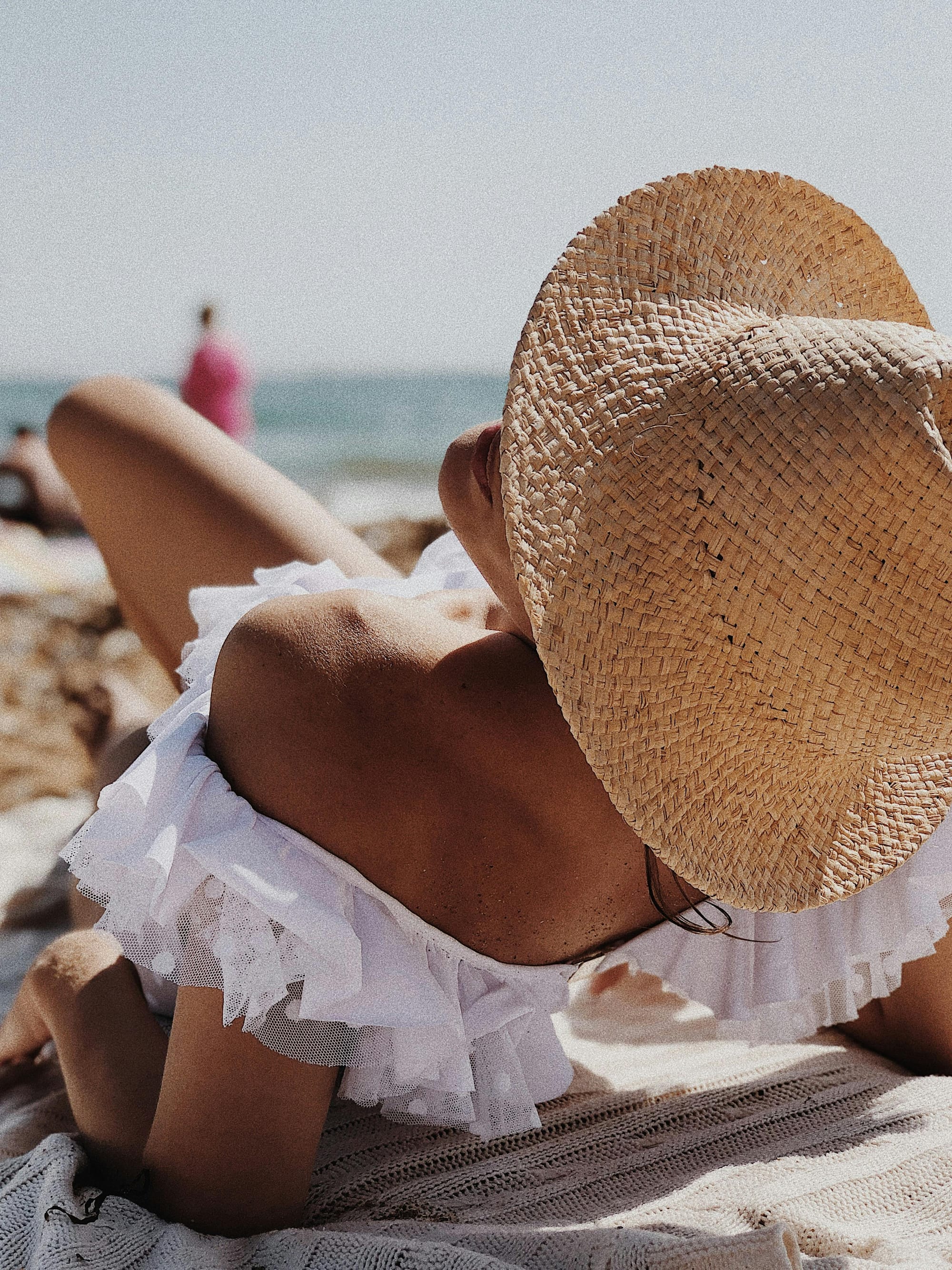 woman lounging on the beach in a summer dress and straw hat