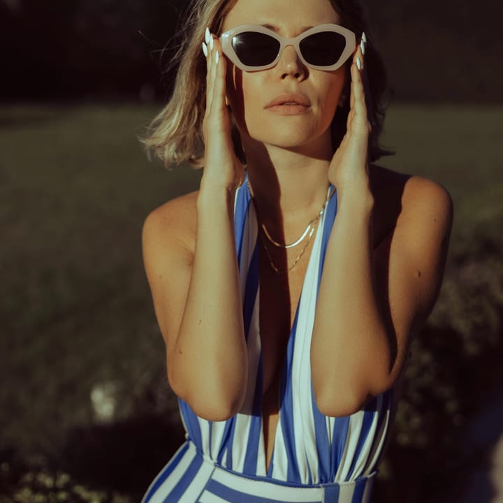 Woman at the beach with striped retro swimsuit, white nailpolish and retro sunglasses